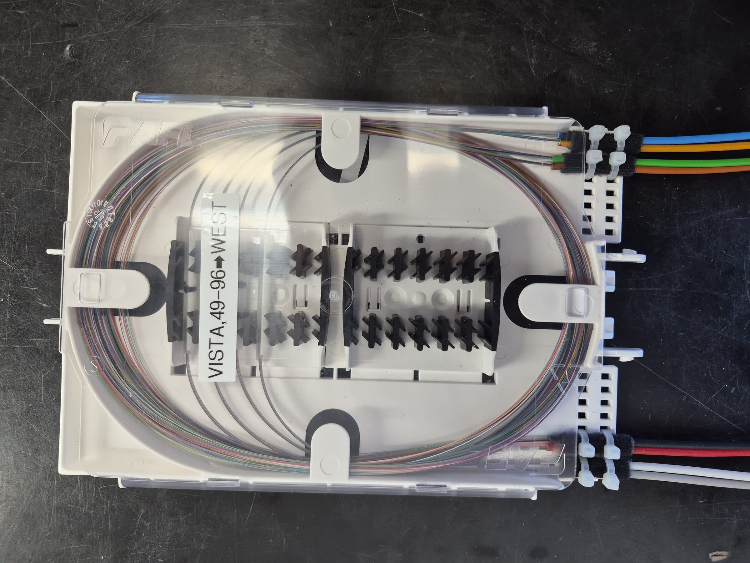 Fiber optic splice enclosure opened on a workbench with color-coded strands routed into labeled splice trays